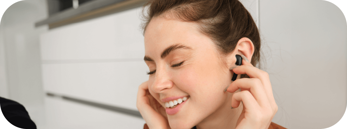 Eine junge Frau hört lächelnd mit geschlossenen Augen Musik mit Ohrstöpseln